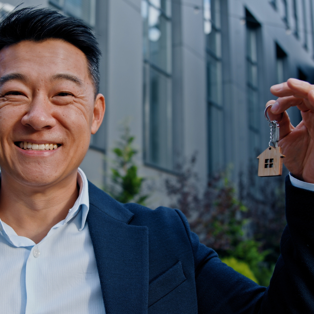 Smiling man holding a key with a house-shaped keyring outside a modern building representing expert guidance on commercial leases and tenancies by Martin Shepherd Solicitors in Hertford, Potters Bar, and North Finchley.