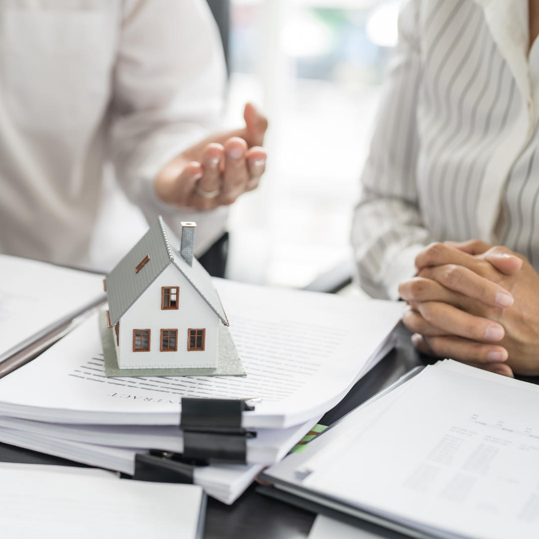 Two people discussing legal documents beside a model house, illustrating the property law services offered by Martin Shepherd Solicitors to resolve ownership, rental and inheritance disputes across Potters Bar, Hertford and North Finchley.